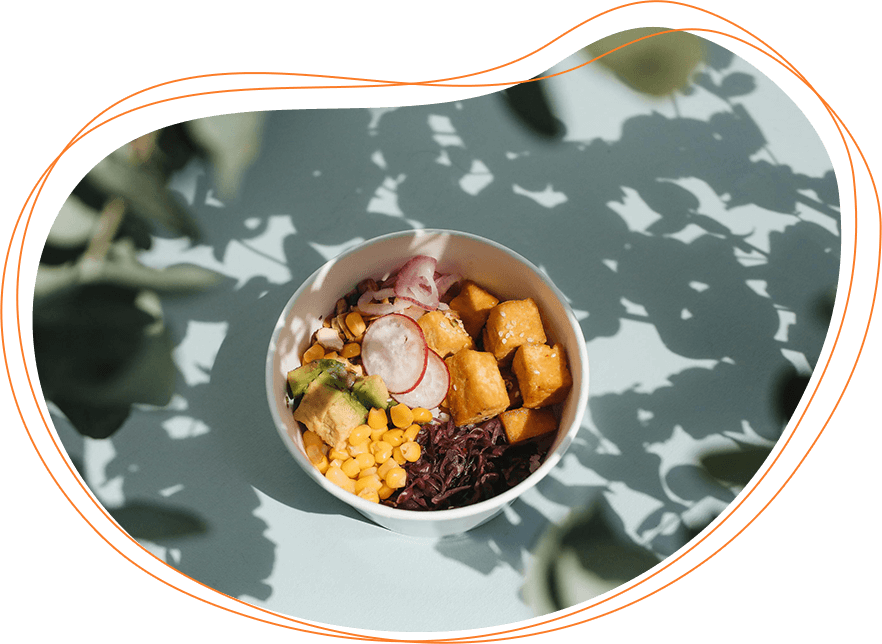 A bowl of healthy salad with corn, radishes, avocado, and rice on a table, shadow patterns from leaves overhead.