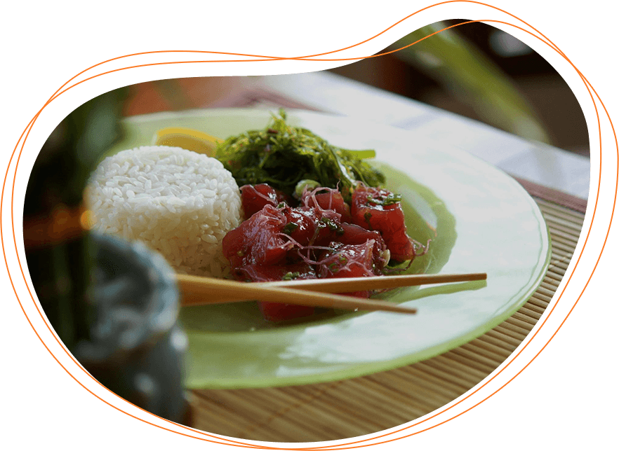 A plate of poke with rice, chopped raw tuna, and seaweed salad, served on a bamboo mat, with chopsticks resting on the plate.